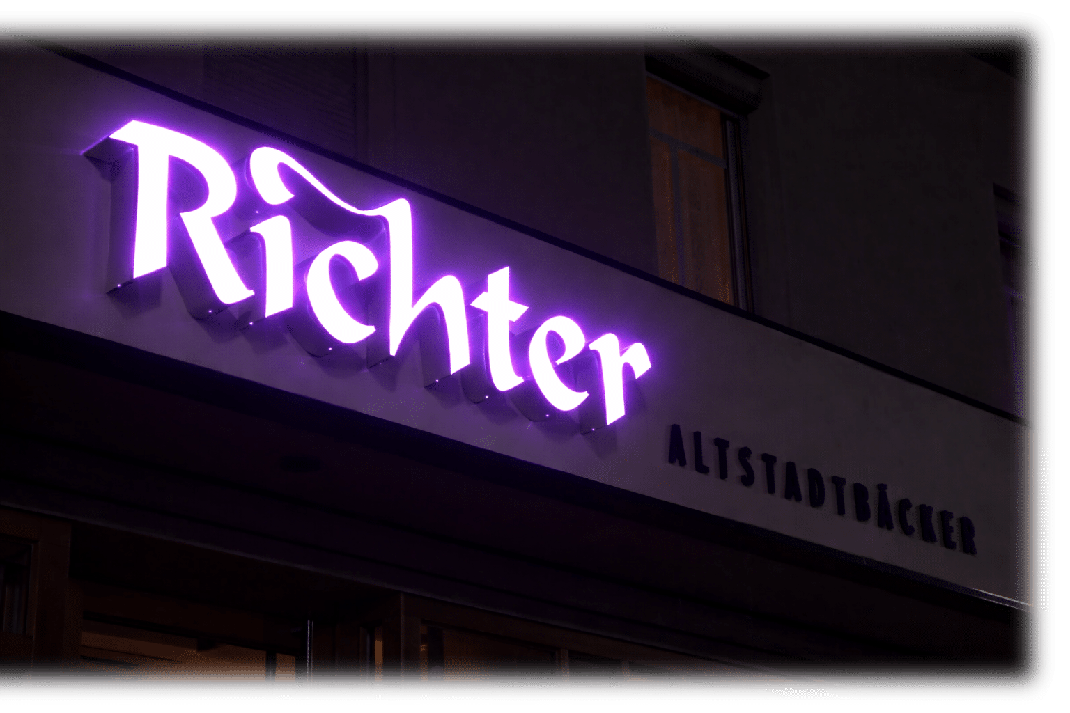 Leuchtender Richter Schriftzug an der Fassade der Altstadtbäckerei bei Nacht – moderne Lichtwerbung mit stilvoller LED-Beleuchtung.