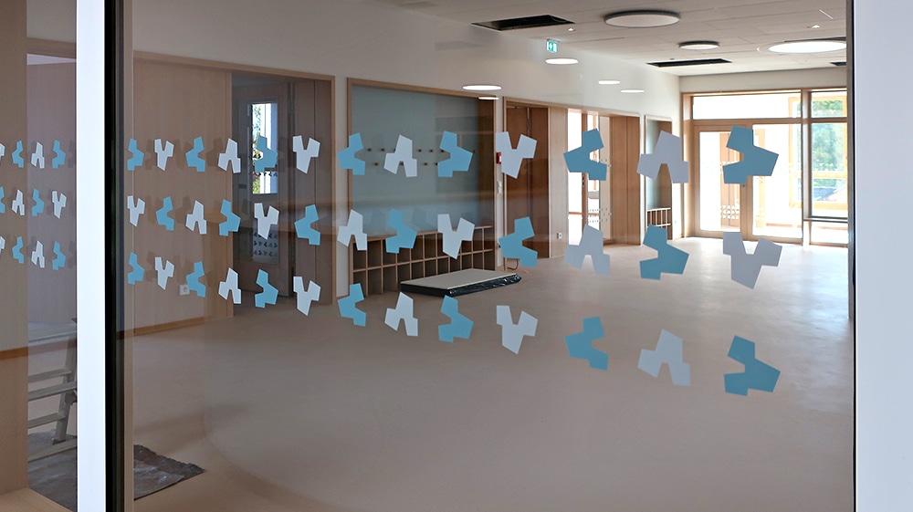 Flur einer Schule mit hellen Glaswänden, die mit blauen, abstrakten Durchlaufschutz-Folien in verschiedenen Mustern beklebt sind.